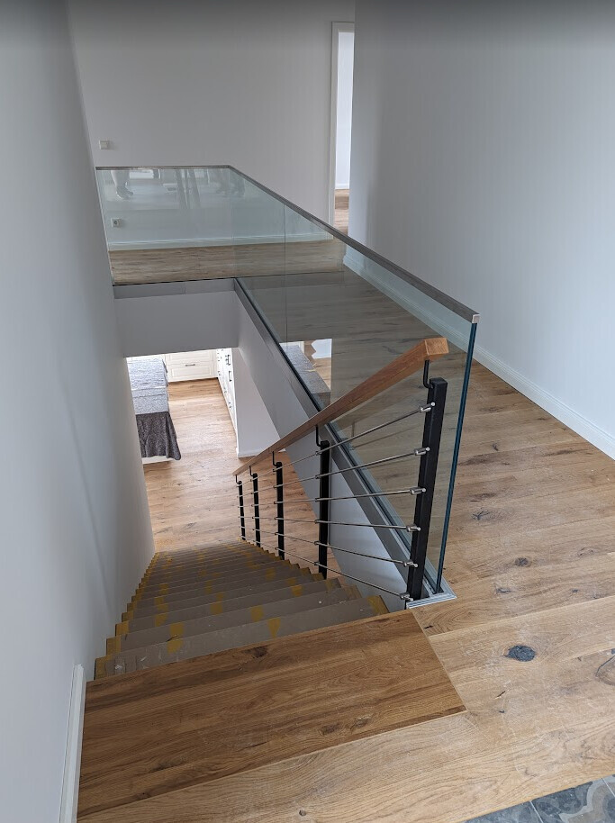 Moderne Treppe mit Glas- und Holzgeländer, Holzboden, offener Aufgang zu mehreren Ebenen.