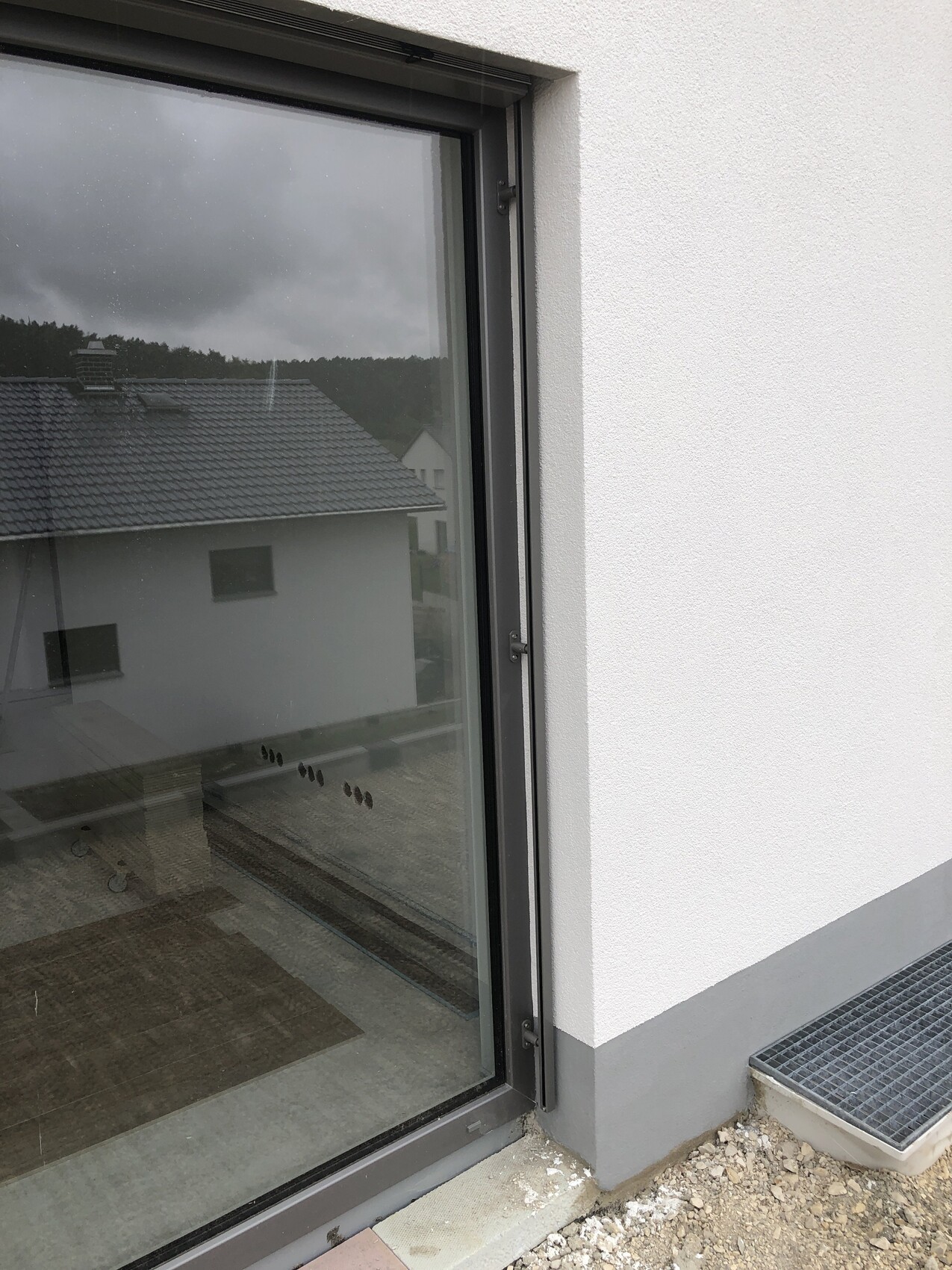 Außenansicht: Glas-Tür in grauem Metallrahmen vor weißer Fassade, Boden mit Metallrost