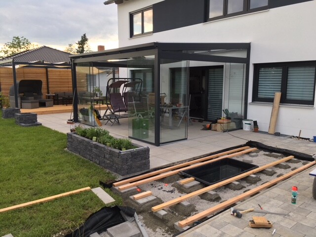 Moderne Glas-Terrassenveranda am Haus; Bauarbeiten im Hof, Baugrube und Holzbalken