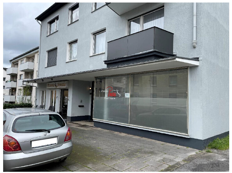 Außenansicht eines grauen Wohn- und Geschäftshauses mit großer Ladenfront und geparktem Auto.