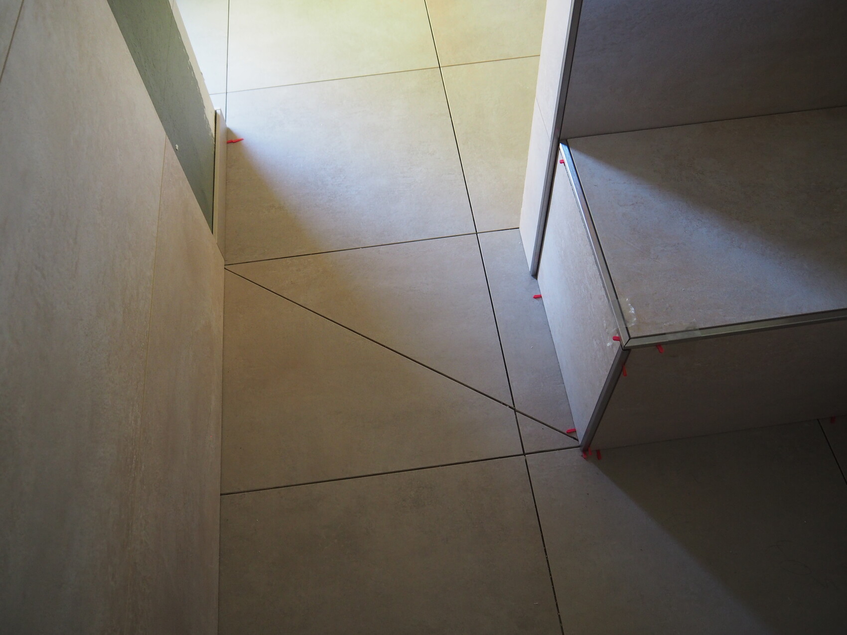 Moderne graue Bodenfliesen in einer Ecke; rechts ein Möbelstück, rote Fliesenspacer sichtbar.