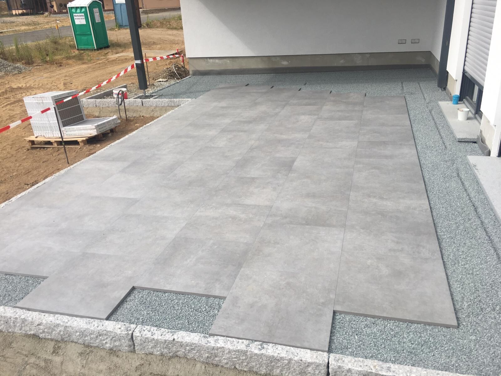 Verlegte graue Terrassenplatten vor dem Haus; Baustelle mit Absperrband, Paletten.
