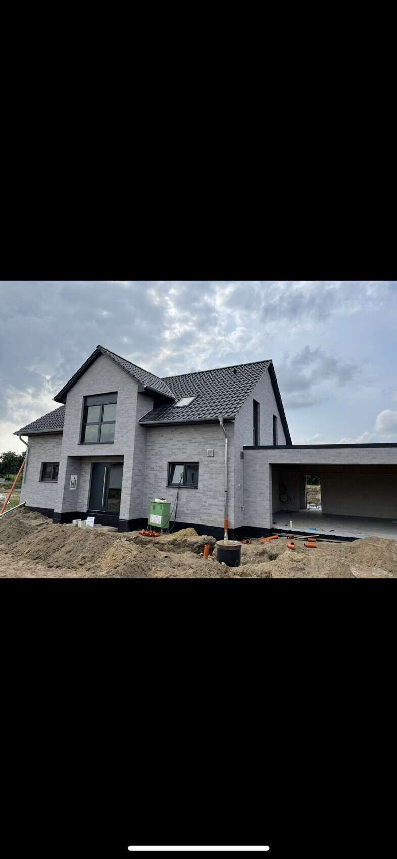 Modernes graues Einfamilienhaus im Bau mit Garage und Baustellenequipment davor