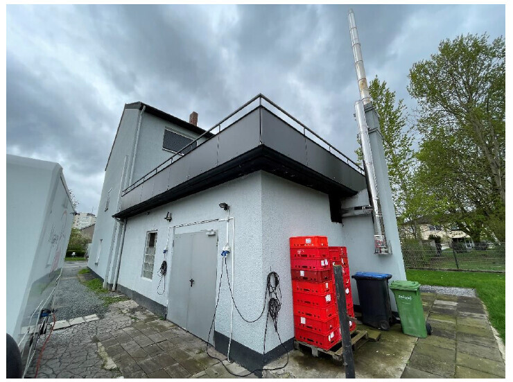 Außenansicht eines Industriegebäudes mit rotem Kistenstapel, Kabeln und Mülltonnen.