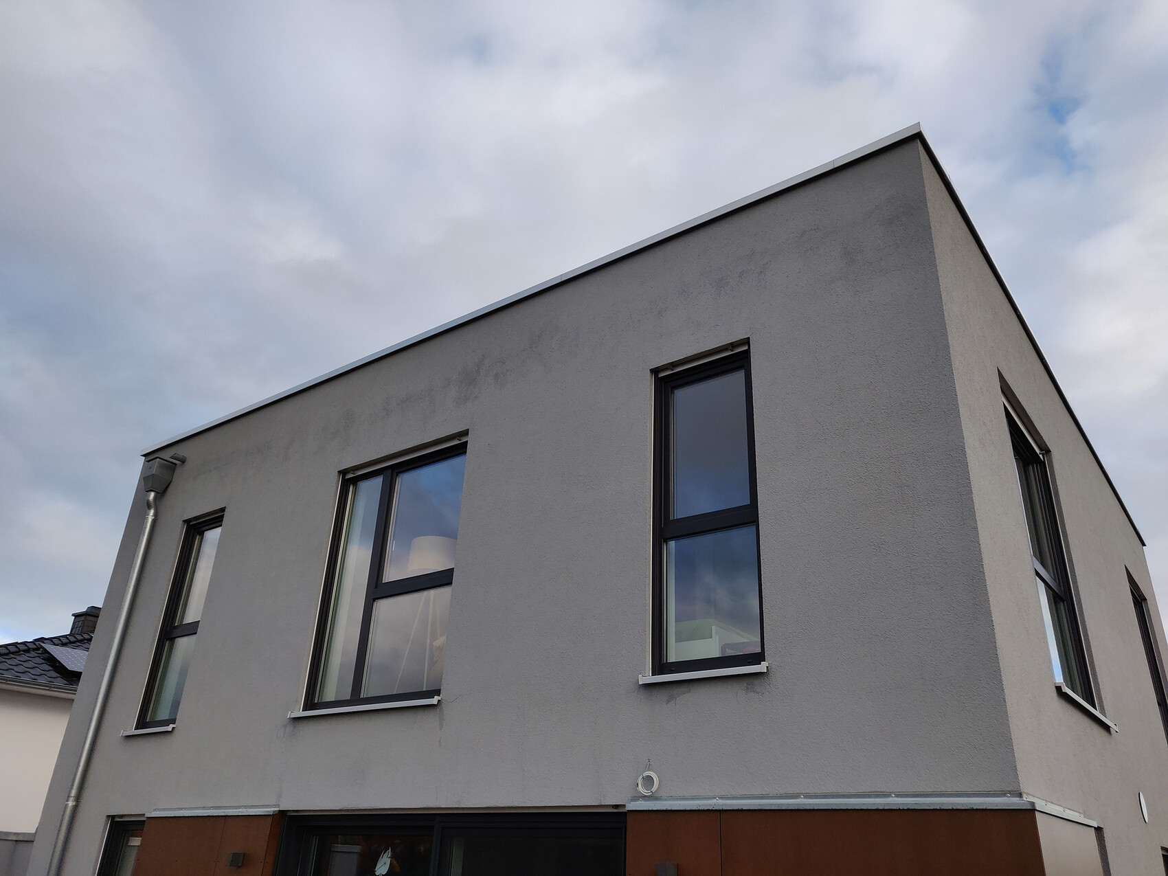 Moderne graue Hausfassade mit großen rechteckigen Fenstern an einer Ecke
