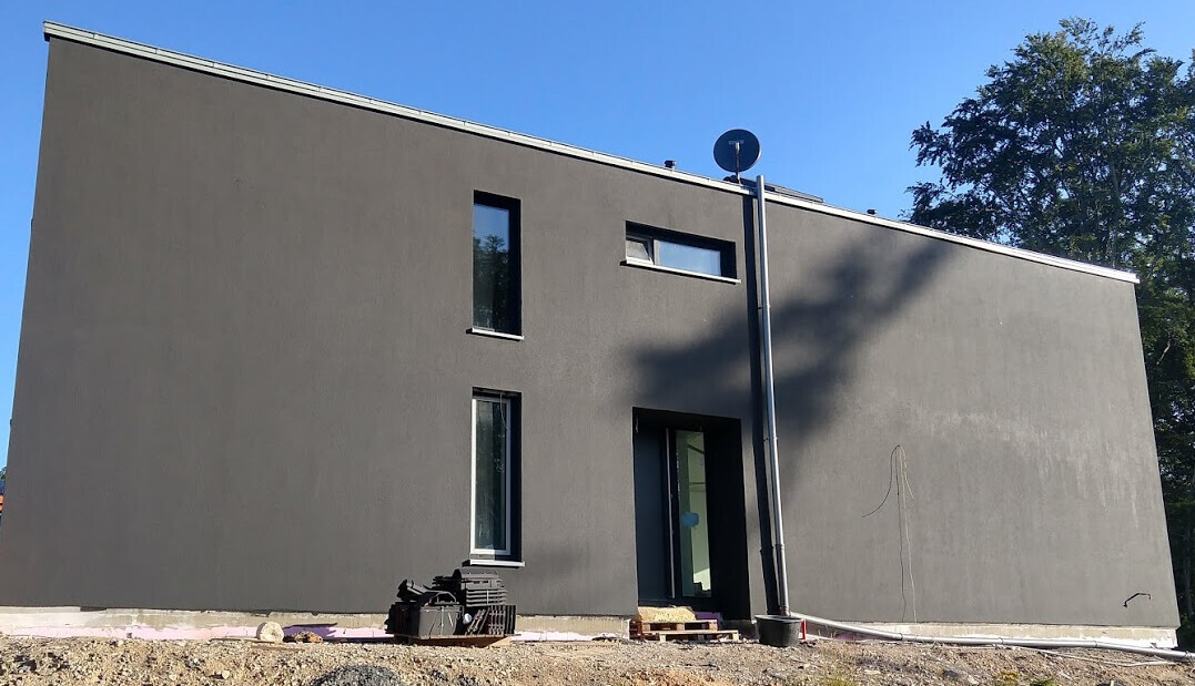 Moderne graue Hausfassade eines Neubaus, Außenansicht mit Eingangstür.