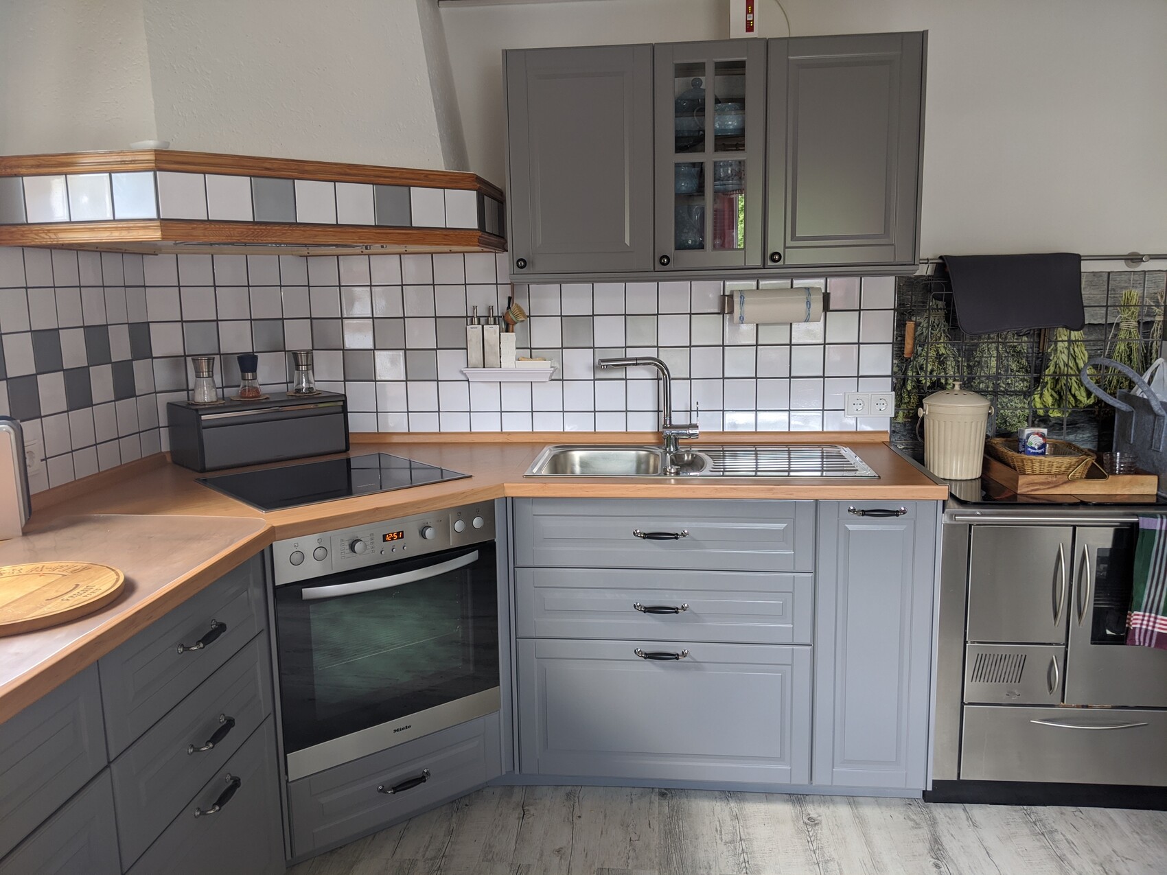 Moderne Küche mit grauen Schränken, Spüle, Herd und Backofen vor einer Fliesenwand.