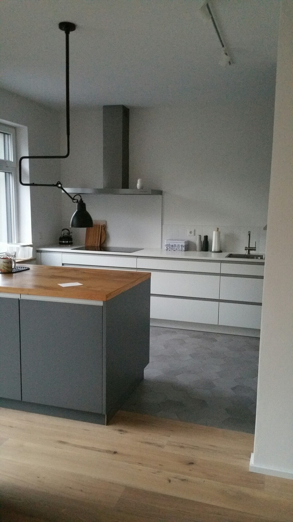 Moderne Küche mit grauen Unterschränken, Holzinsel, schwarze Industrie-Lampe, Spüle.