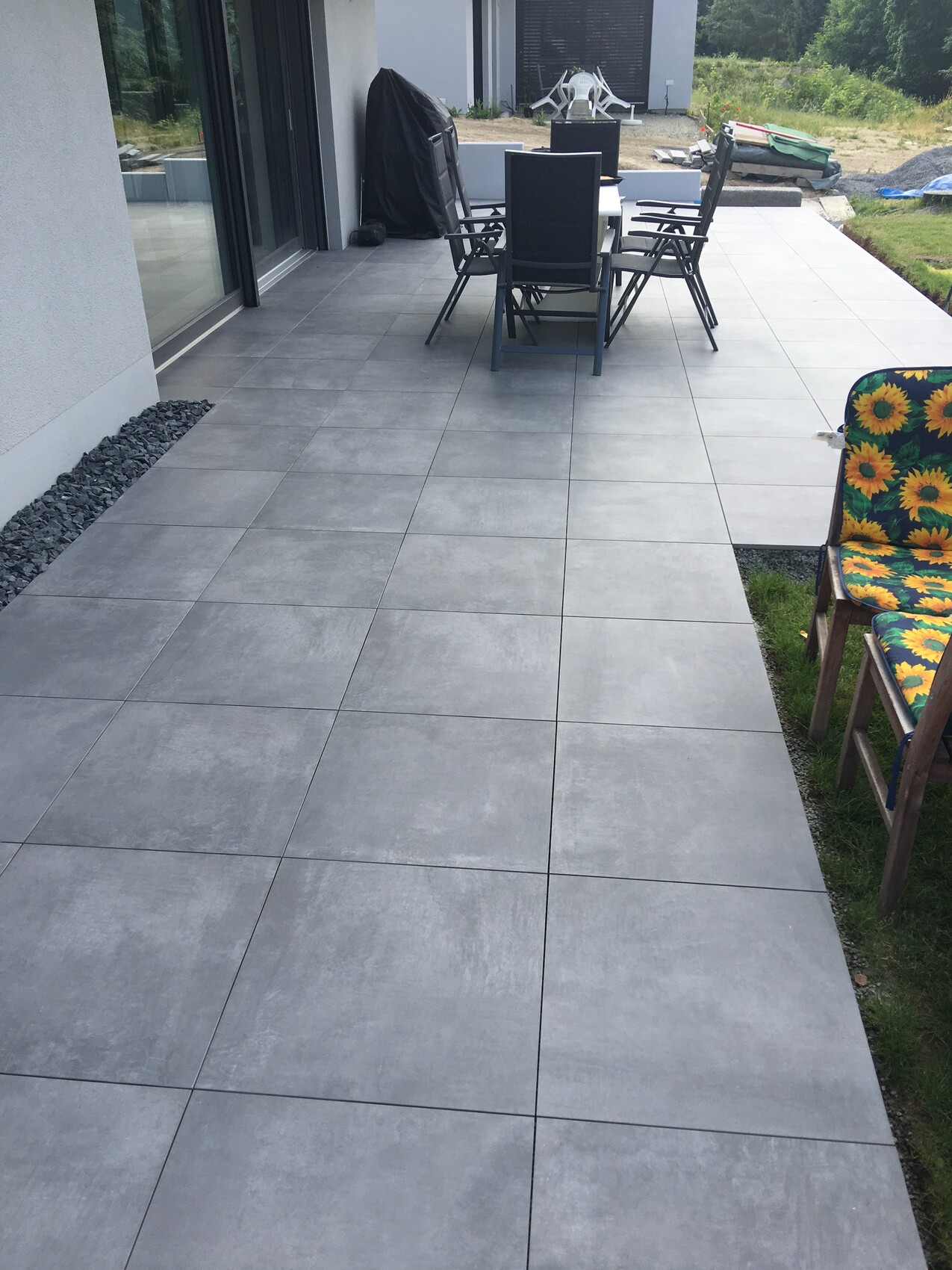 Grau gepflasterte Terrasse mit Esstisch und Stühlen vor dem Haus, Garten im Hintergrund.
