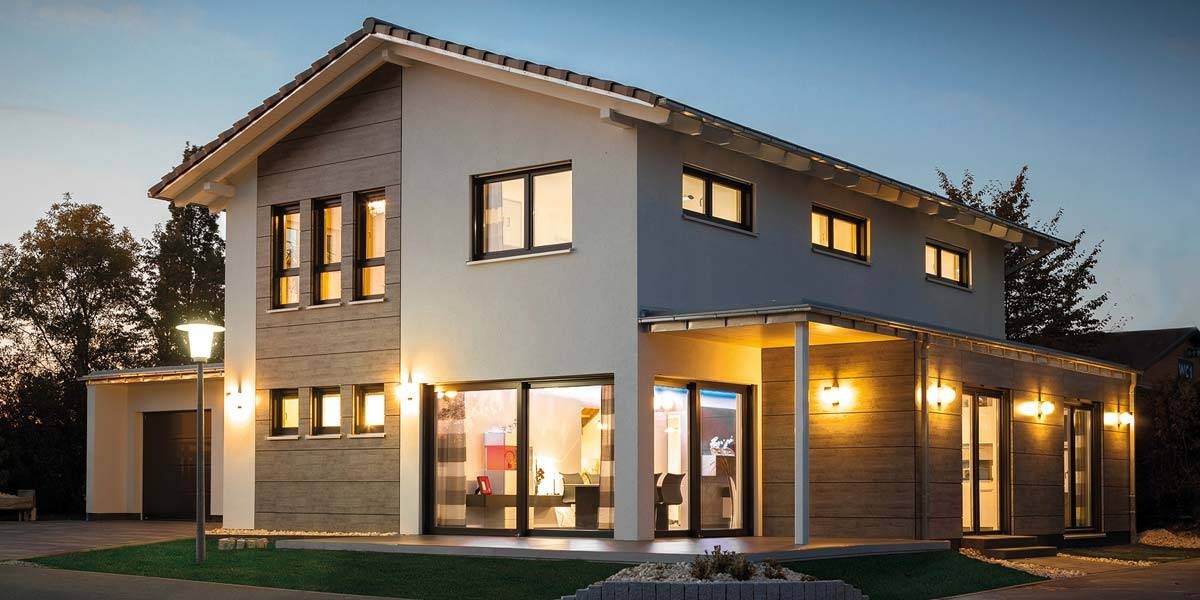 Modernes zweistöckiges Haus mit großen Fensterfronten, warm beleuchtetem Innenraum und Außenlampen