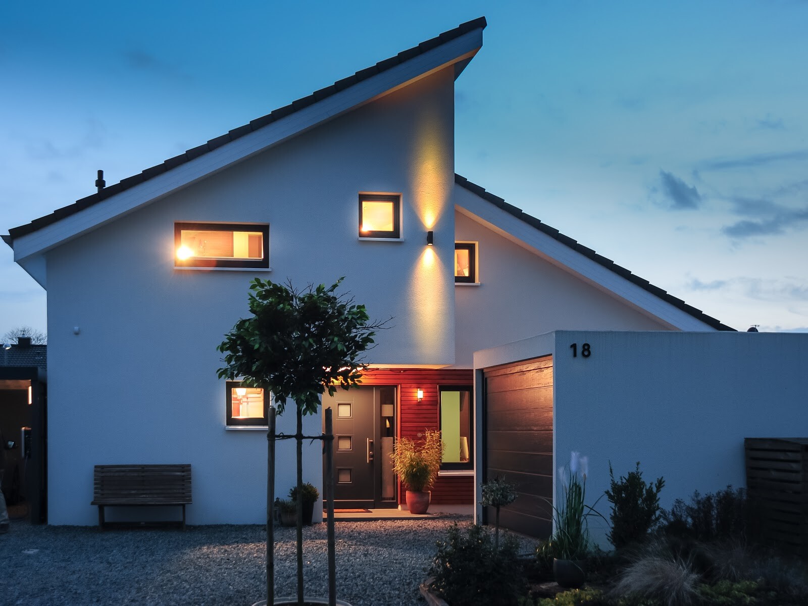 Moderne Einfamilienhaus-Fassade mit Garage und beleuchteten Fenstern bei Dämmerung