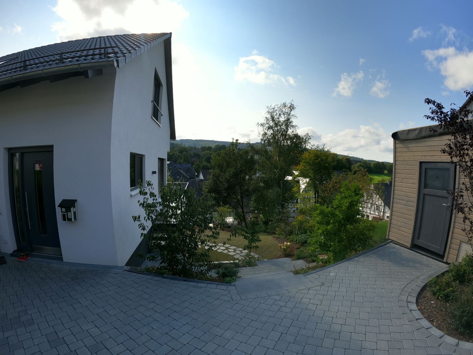 Weiße Villa links, gepflasterter Hof, Garten und Nebengebäude rechts; Blick ins grüne Tal