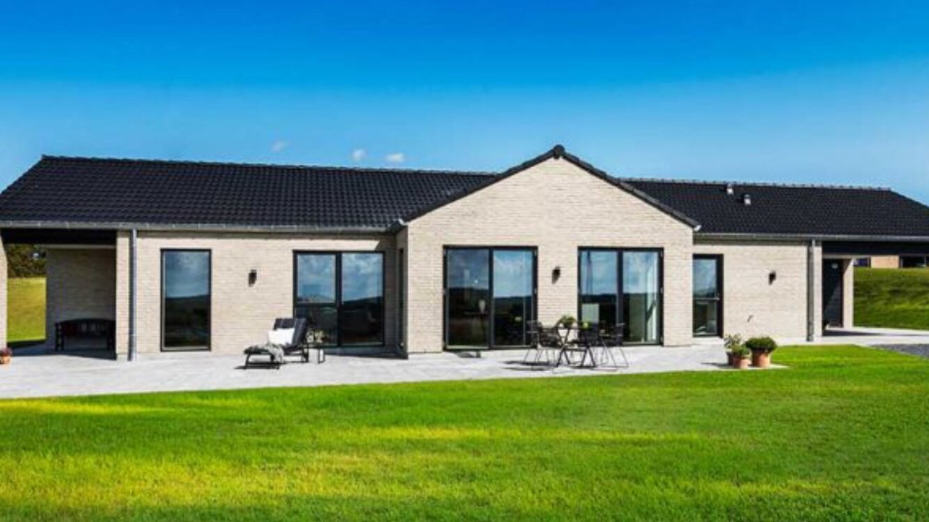 Modernes Einfamilienhaus mit Glasfronten, Terrasse und grünem Rasen unter blauem Himmel.