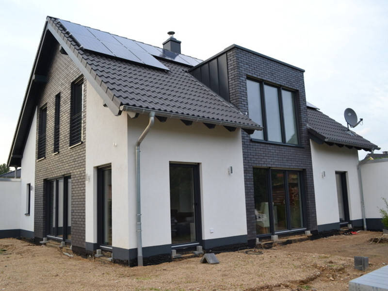 Modernes Einfamilienhaus mit weißen Fassaden, dunklen Akzenten und Solaranlagen auf dem Dach