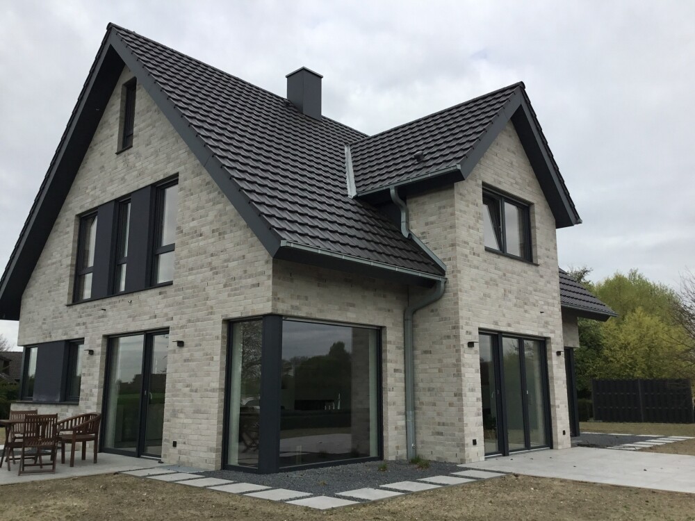Modernes zweistöckiges Haus mit Backsteinfassade, großen Glasfenstern und Terrasse.