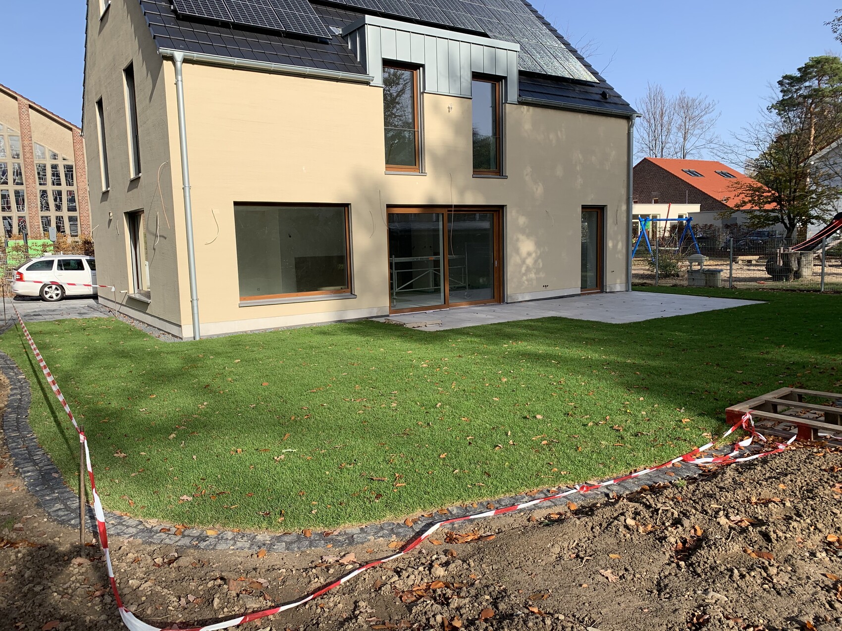 Modernes Haus mit großen Fenstern, Terrasse, grünem Rasen und Bauabsperrband.