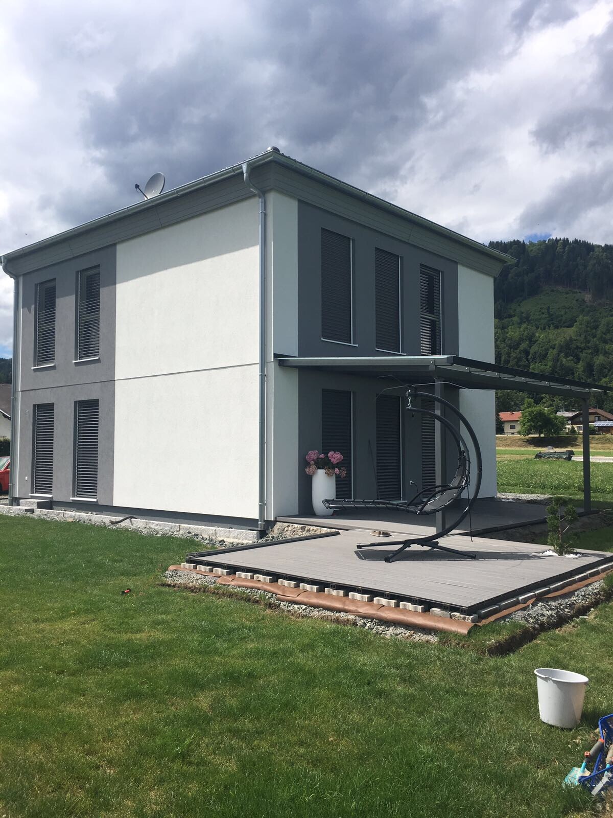 Modernes zweistöckiges Haus mit grauer Fassade und Terrasse mit Hängesessel.