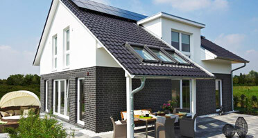 Moderne weiße Hausfront mit dunkler Steinoptik, Terrasse und Garten.