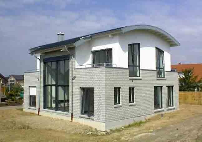Modernes Einfamilienhaus mit weißer Fassade, grauer Steinoptik und großen Fenstern auf Baugrund.