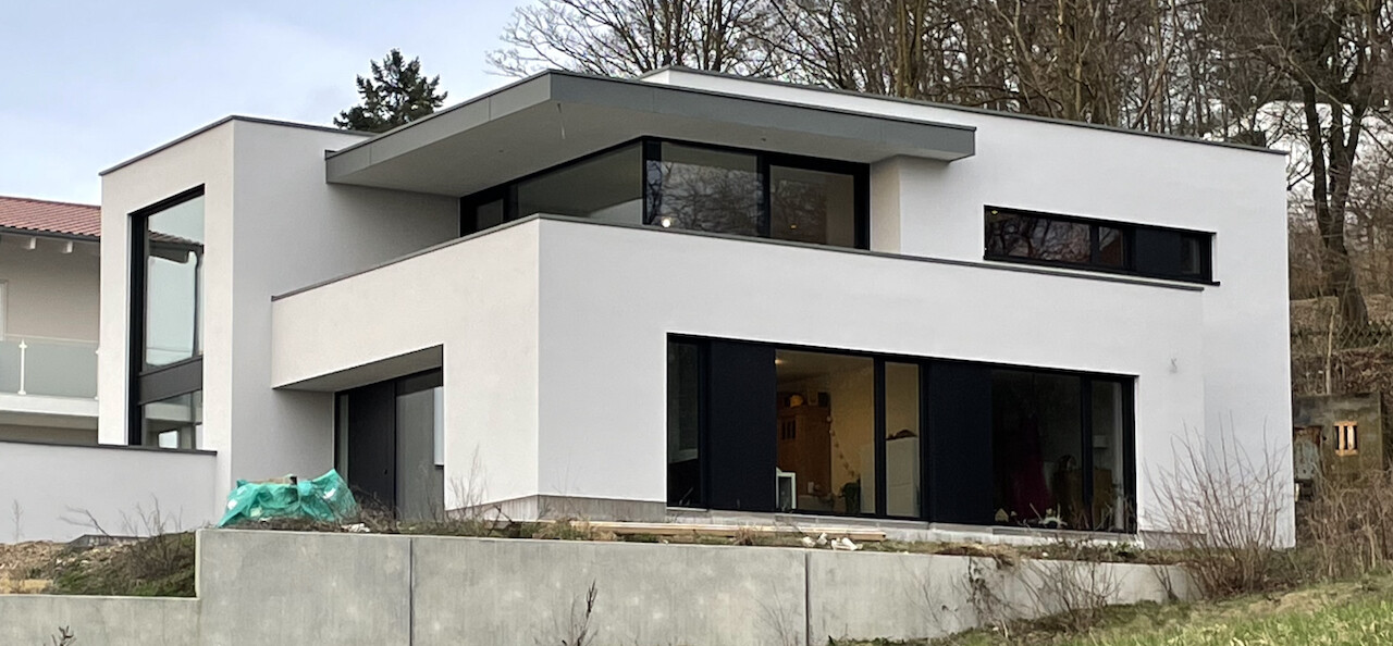 Modernes, weißes, zweigeschossiges Haus mit großen Glasfronten und flachem Dach.