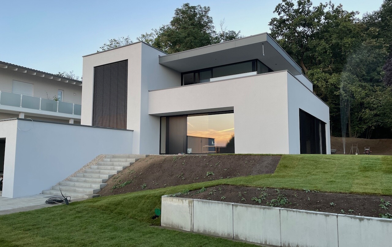 Moderne weiße Villa mit großen Fenstern, Treppenstufen und Sonnenuntergang im Fenster.