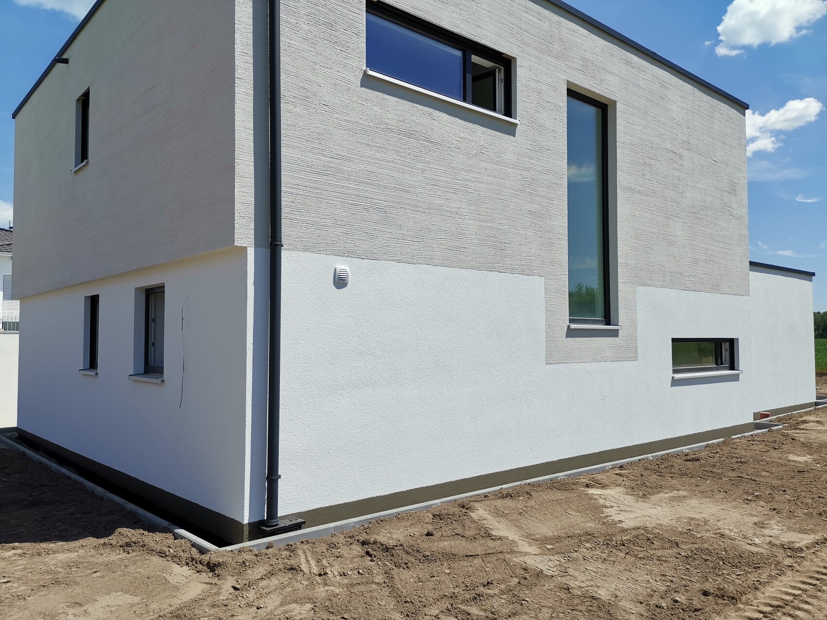 Modernes zweistöckiges Haus mit weißer Fassade und grauer Putzstruktur, Bauumgebung.
