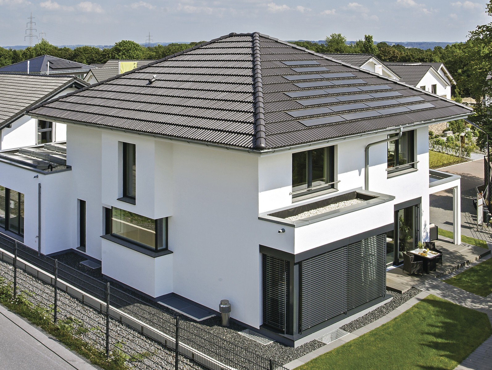 Moderne weiße Villa mit dunklem Dach, großen Fenstern und Terrasse im Garten.
