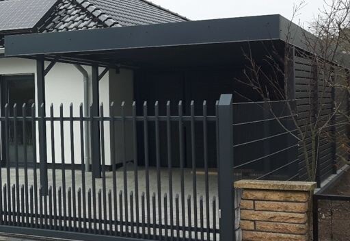 Moderne Hausfront mit dunklem Carport, Metallzaun und Zugangsterrasse