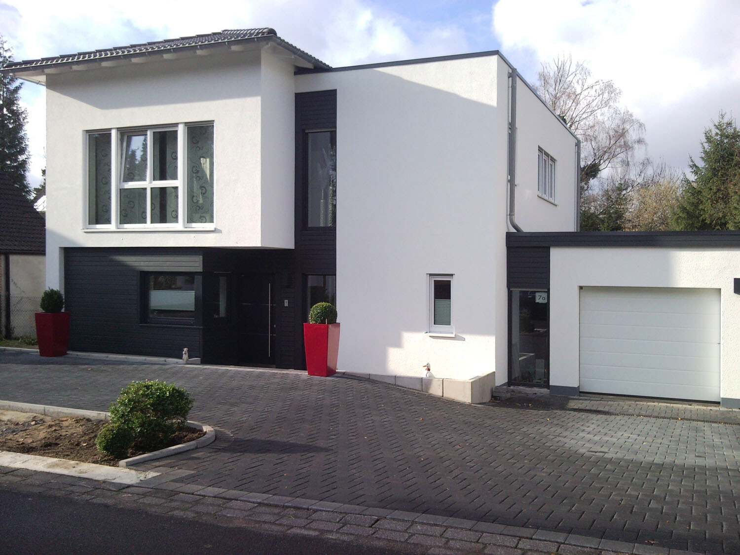 Modernes zweigeschossiges Haus mit weißer Fassade, schwarzer Verkleidung, Fensterfront und Garage.
