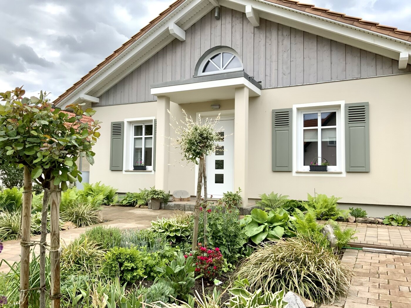 Vorderansicht eines Einfamilienhauses mit grauen Fensterläden und Garten.