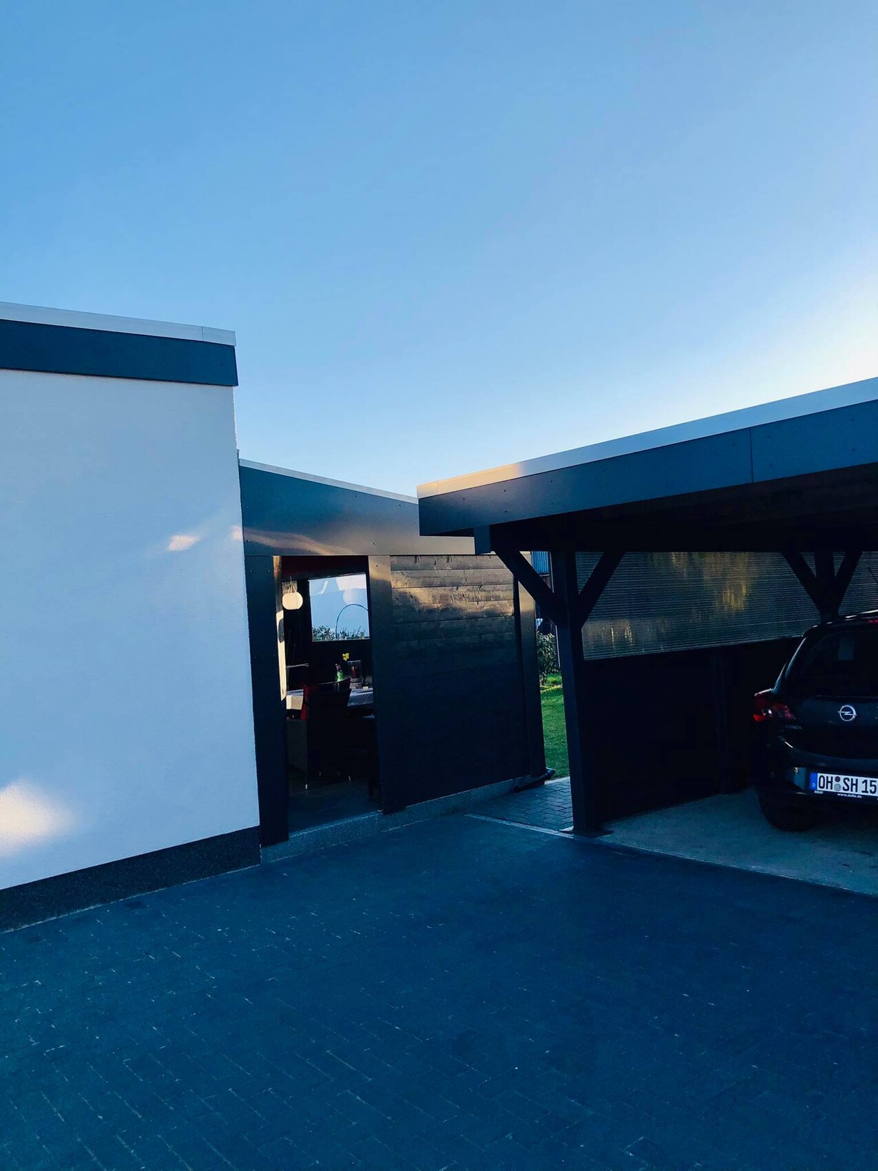 Moderne Hausfront mit weißer Wand, offener Eingang, dunklem Carport und geparktem Auto.
