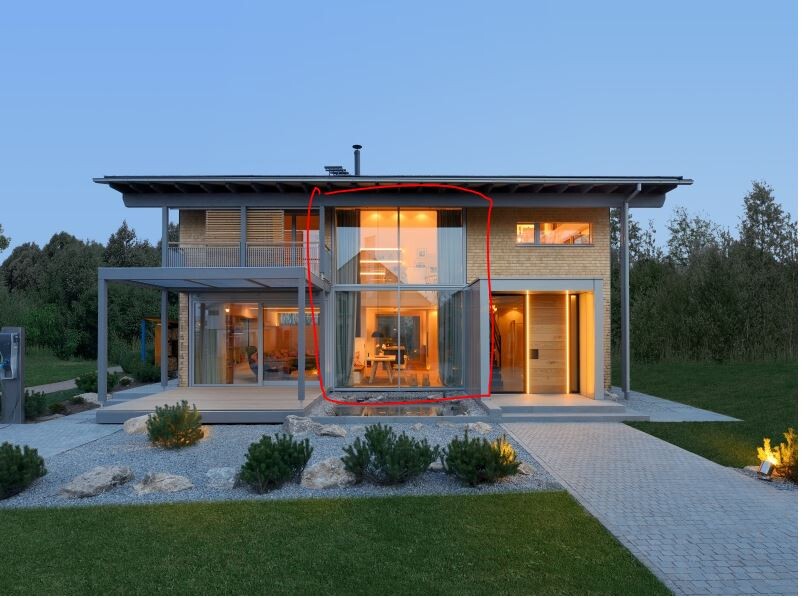 Modernes zweistöckiges Haus mit einem verglasten Wintergarten in der Mitte, beleuchtet.