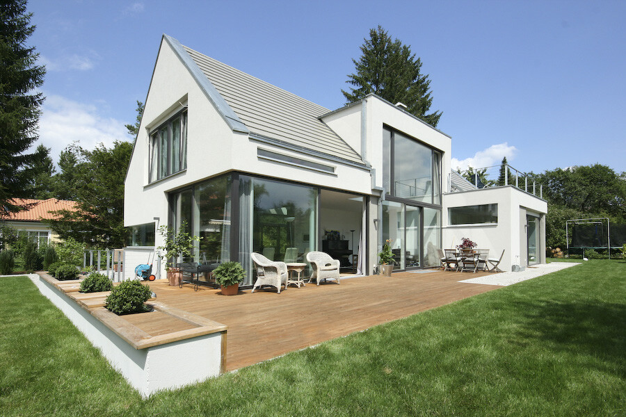 Moderne weiße Villa mit großen Glasfronten, Holzterrasse und Gartenmöbel.