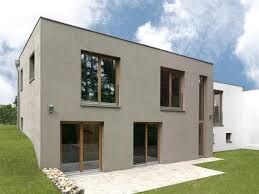 Modernes zweistöckiges Haus mit heller Fassade, großen Fenstern und Terrasse im Grünen.