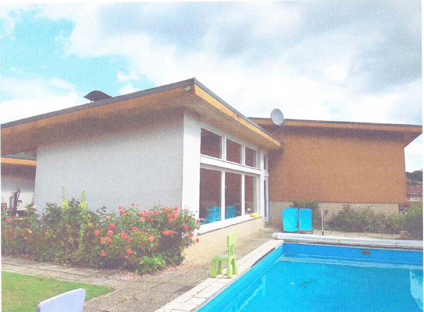 Modernes Einfamilienhaus mit Glasfront, blauem Pool, blühendem Garten und zwei Liegen.