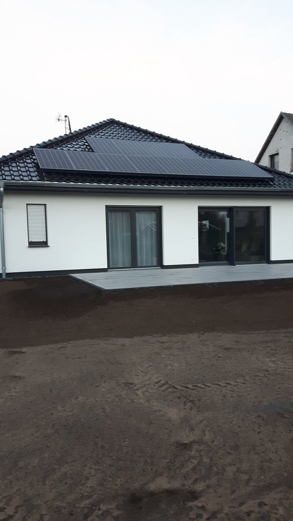 Modernes Einfamilienhaus mit weißen Wänden, Glas-Schiebetüren und Solarmodulen auf dem Dach.