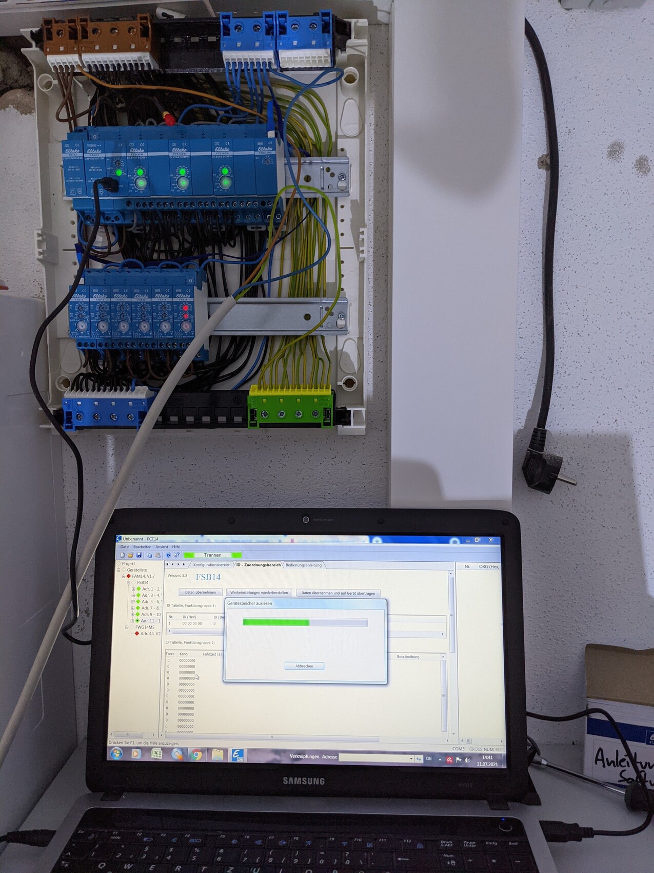 Schalttafel mit blauen Relaismodulen und vielen Kabeln; Laptop mit Software-Fortschritt