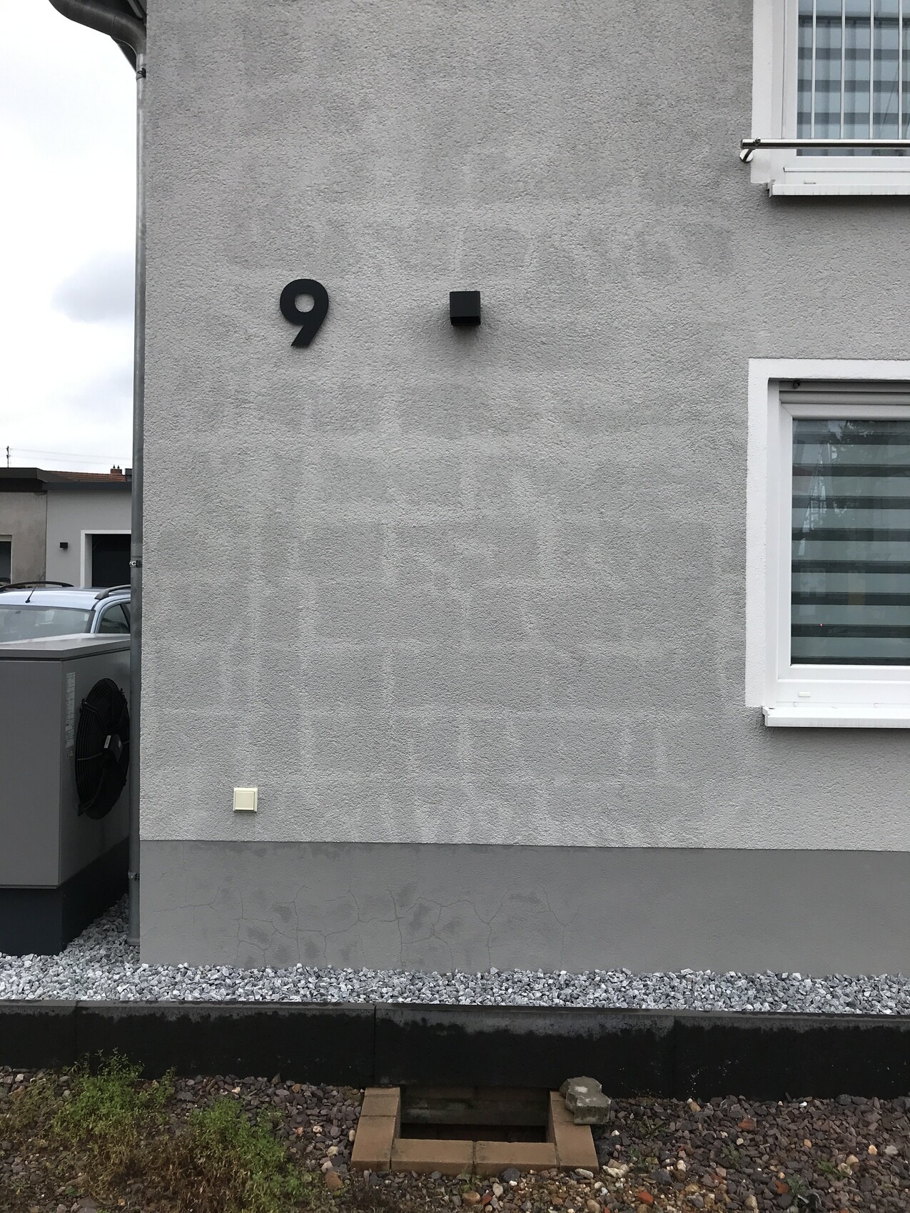 Außenwand eines Hauses mit der Nr. 9, kleinem schwarzen Würfel und Fenster rechts.
