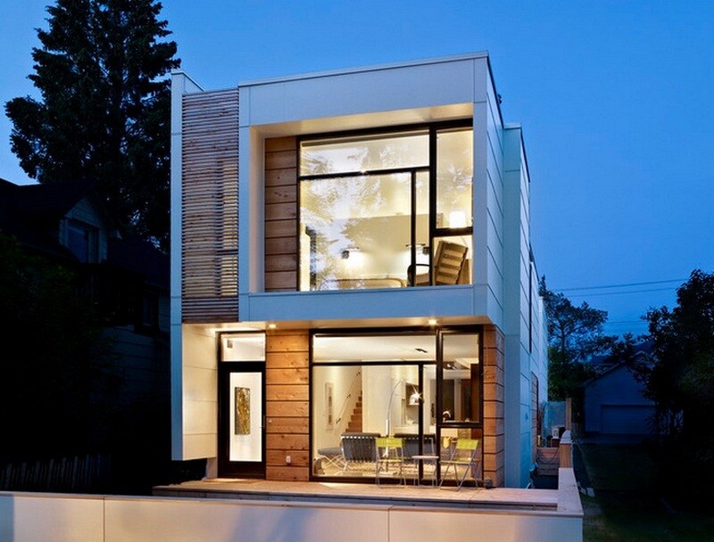 Modernes zweistöckiges Haus mit großen Glasfronten und beleuchtetem Innenraum.