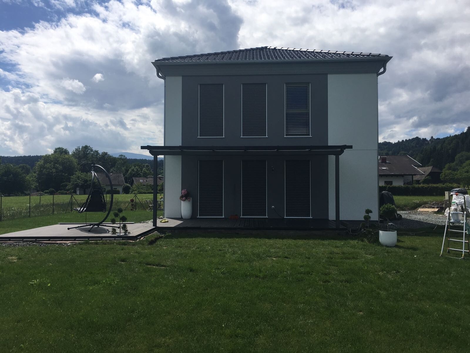 Zweistöckiges modernes Haus mit grauer Fassade, dunkler Veranda und gepflegtem Garten.