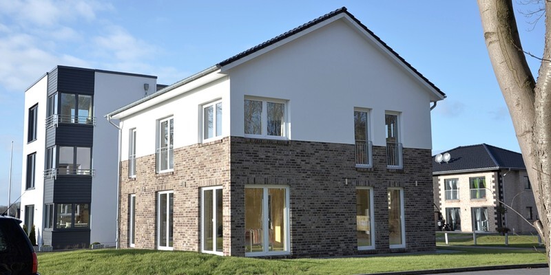Zweistöckiges Einfamilienhaus mit weißer Fassade oben und Ziegelband unten, große Fenster.