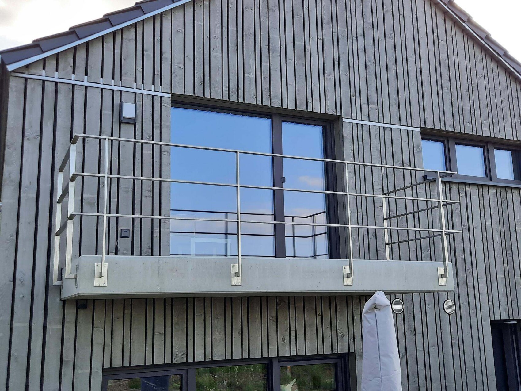 Moderne Holzfassade mit vertikalen Dielen; Balkon aus Beton mit Metallgeländer und Glasfenstern