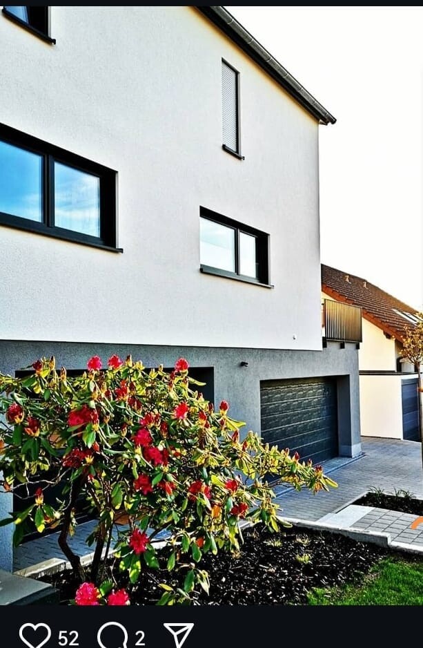 Moderne weiße Hausfassade mit grauer Garage, schwarzen Fenstern und blühendem Garten