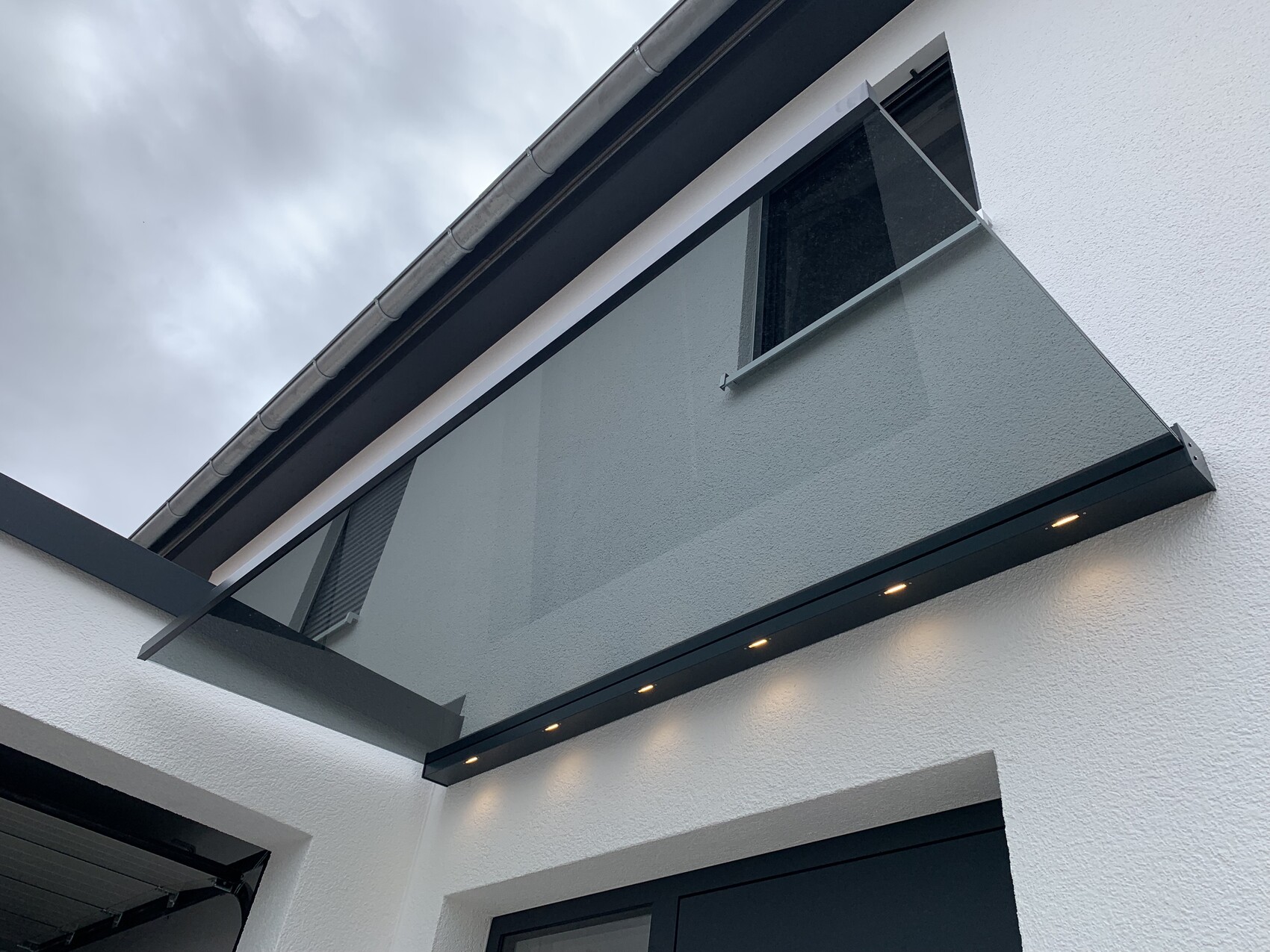 Moderne weiße Hausfassade mit schwebendem Glasbalkon und LED-Lichtleisten.
