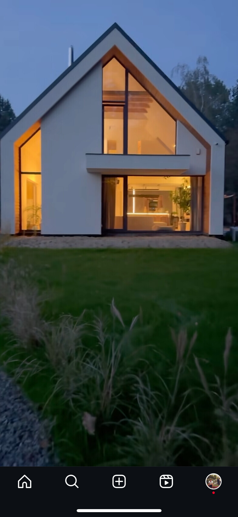 Moderne weiße A-Frame Hausfront mit großen Glasfenstern, warmes Innenlicht.