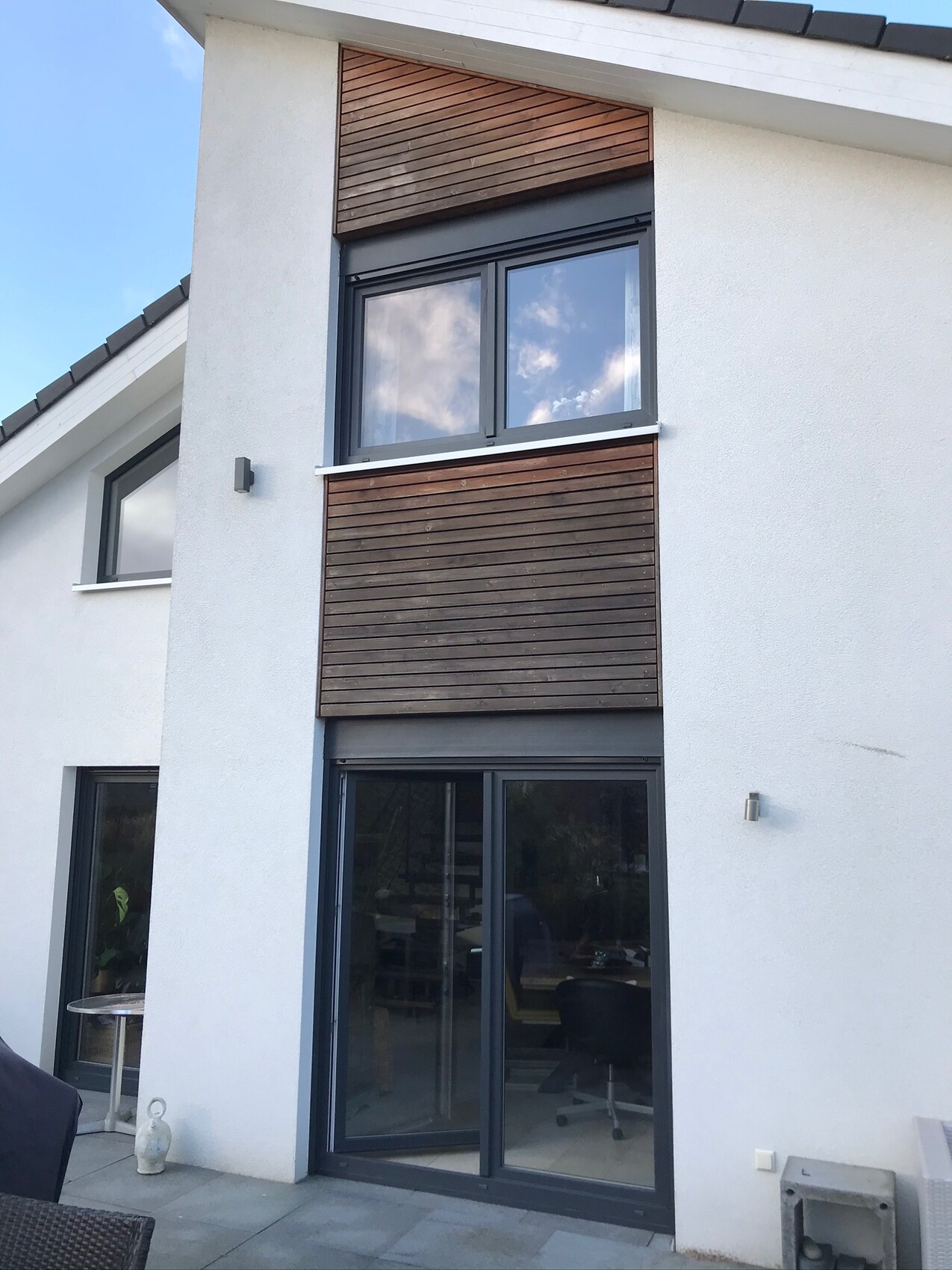 Moderne weiße Fassade mit großen Glas-Schiebetüren im Erdgeschoss und Holzlamellen-Verkleidung.