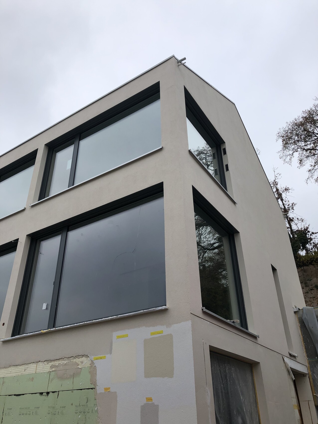 Modernes zweistöckiges Haus mit großen Glasfenstern; Bauarbeiten an der Fassade.