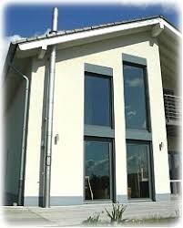 Außenansicht eines modernen Hauses mit großen Glasfenstern und weißer Fassade.