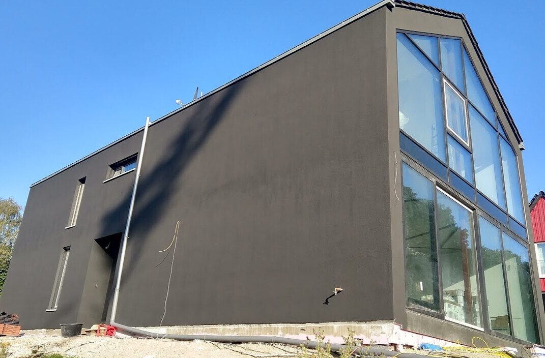 Modernes graues Gebäude mit großer Glasfassade; Bauzubehör und Materialreste am Boden.