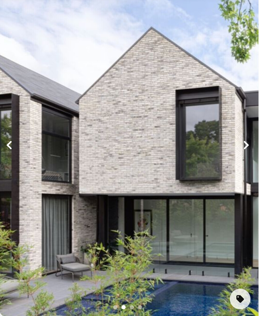 Moderne villaähnliche Hausfront aus hellem Backstein, große Glasfronten, Pool im Vorgarten.